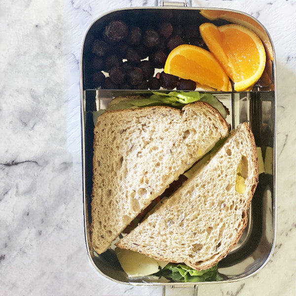 Stainless steel rectangular lunch box with removable divider, includes sandwich and cut fruit