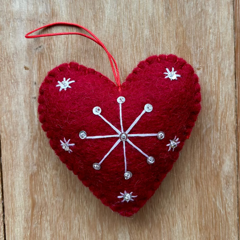 Red heart-shaped ornament with white snowflake design on a wooden surface