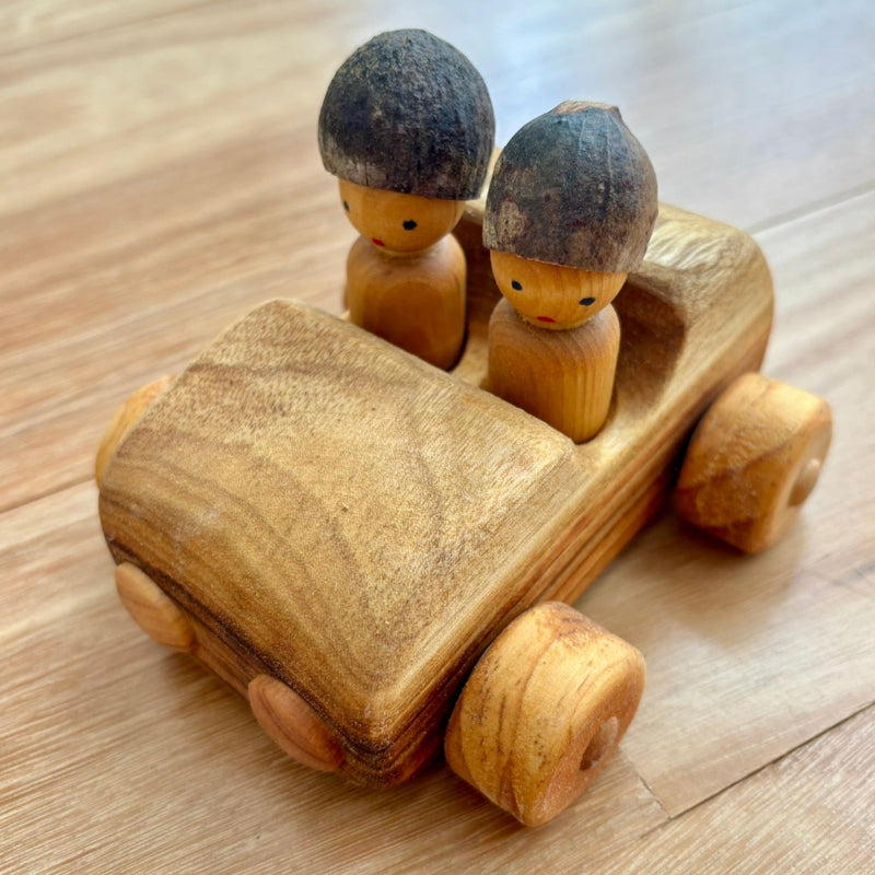 Wooden toy car (front view) with two small wooden figures on a wooden surface