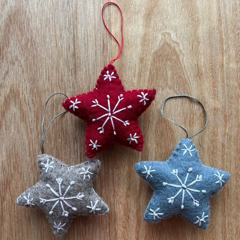 Three star-shaped Christmas ornaments with snowflake patterns made from wool felt.