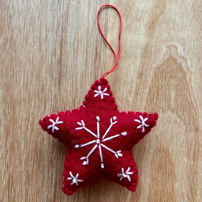 Red star-shaped ornament with white snowflake patterns on a wooden surface