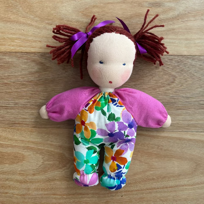 Handmade Steiner / Waldorf doll with a colorful floral outfit on a wooden surface
