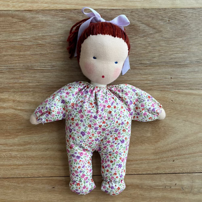 Small handcrafted Steiner/ Waldorf doll with floral dress on a wooden surface