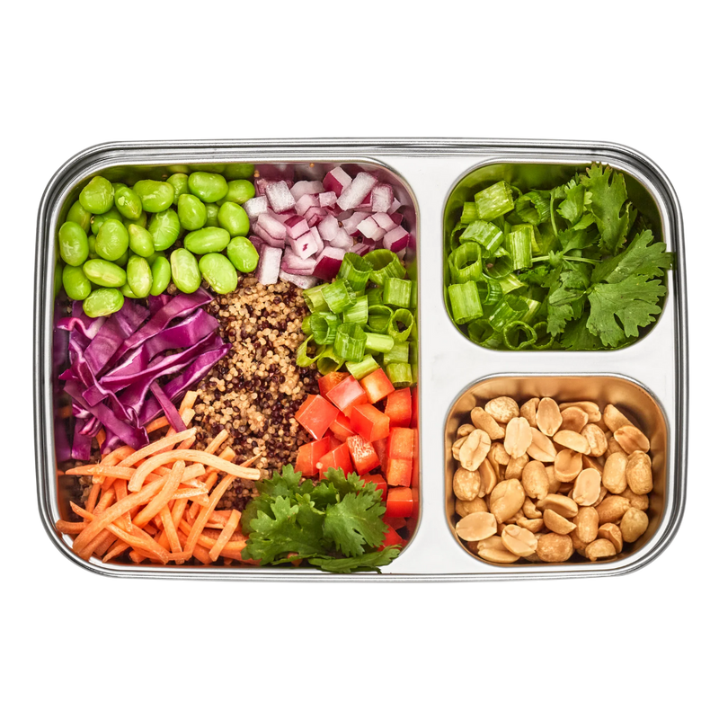 Stainless steel 3 compartment lunchbox with various chopped vegetables and nuts on a white background