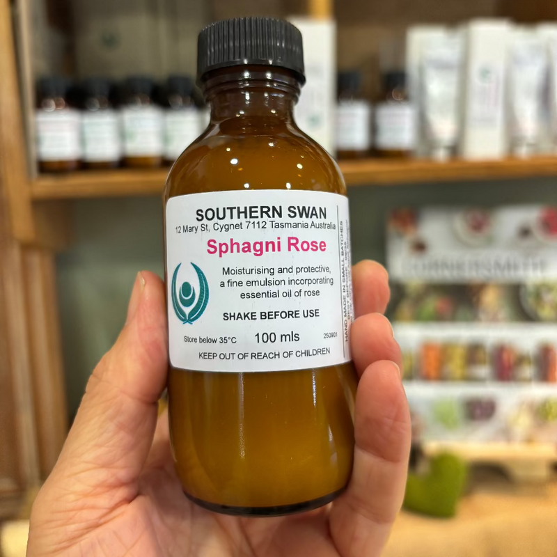 Hand holding a bottle of Southern Swan Sphagni Rose essential oil with a blurred store shelf in the background.